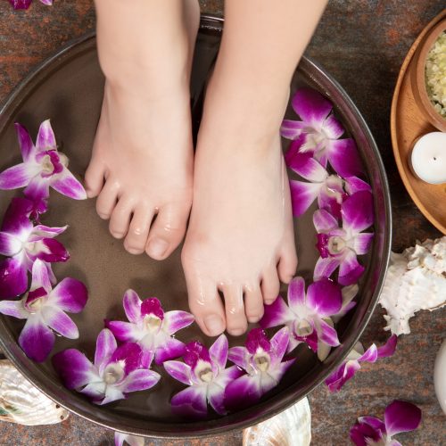closeup view of woman soaking her hand and feet in dish with water and flowers on wooden floor. Spa treatment and product for female feet and hand spa. orchid flowers in ceramic bowl.